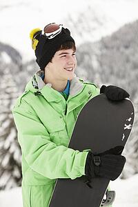 Teenage Boy With Snowboard On Ski Holiday In Mountains