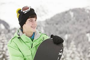 Teenage Boy With Snowboard On Ski Holiday In Mountains