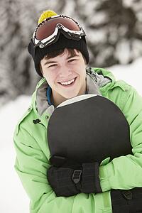 Teenage Boy With Snowboard On Ski Holiday In Mountains