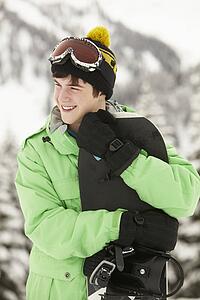 Teenage Boy With Snowboard On Ski Holiday In Mountains