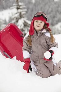 Young Girl Playing In Snow With Sledge On Ski Holiday In Mountains