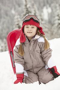 Young Girl Playing In Snow With Sledge On Ski Holiday In Mountains