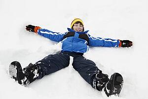 Young Boy Making Snow Angel On Slope