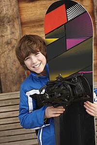 Boy With Snowboard On Ski Holiday In Front Of Wooden Background