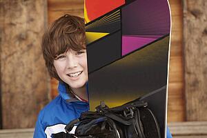 Boy With Snowboard On Ski Holiday In Front Of Wooden Background