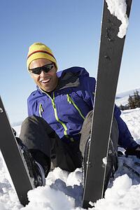 Male Skier Sitting In Snow With After Fall