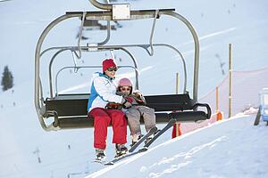 Mother And Daughter Getting Off chair Lift On Ski Holiday In Mountains