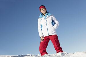 Woman Standing In Snow Wearing Warm Clothes On Ski Holiday In Mountains