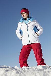 Woman Standing In Snow Wearing Warm Clothes On Ski Holiday In Mountains