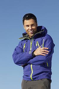 Man Standing In Snow Wearing Warm Clothes On Ski Holiday In Mountains