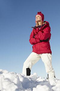 Woman Standing In Snow Wearing Warm Clothes On Ski Holiday In Mountains