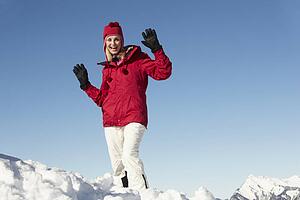 Woman Standing In Snow Wearing Warm Clothes On Ski Holiday In Mountains