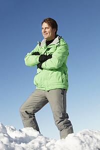 Man Standing In Snow Wearing Warm Clothes On Ski Holiday In Mountains