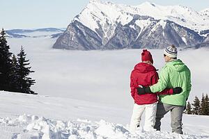 Couple Admiring Mountain View Whilst On Ski Holiday In Mountains