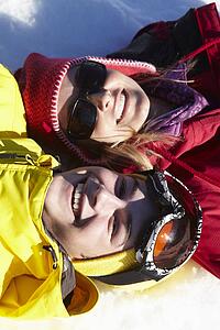 Overhead View Of Mother And Teenage Son Lying In Snow On Ski Holiday In Mountains