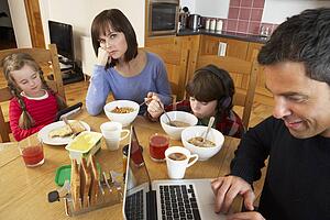 Family Using Gadgets Whilst Eating Breakfast Together In Kitchen