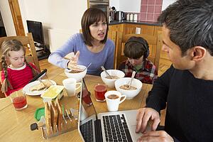 Family Using Gadgets Whilst Eating Breakfast Together In Kitchen