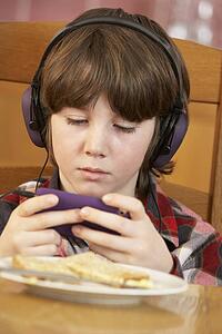 Boy Playing With Hand Held Games Console Whilst Eating Breakfast