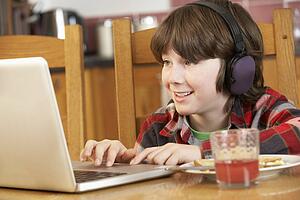 Boy Using Laptop Whilst Eating Breakfast