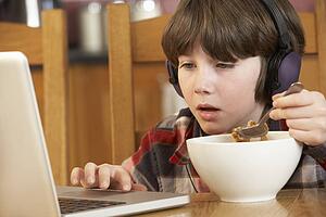 Boy Using Laptop Whilst Eating Breakfast