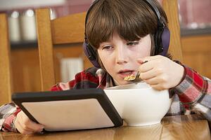 Boy Using Tablet Computer Whilst Eating Breakfast