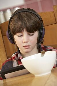 Boy Using Tablet Computer Whilst Eating Breakfast