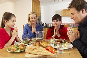 Teenage Family Saying Grace Before Eating Lunch Together In Kitchen