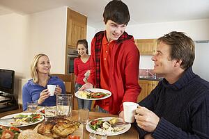 Helpful Teenage Children Serving Food To Parents In Kitchen