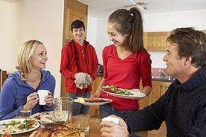 Helpful Teenage Children Serving Food To Parents In Kitchen