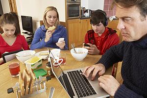 Teenage Family Using Gadgets Whilst Eating Breakfast Together In Kitchen