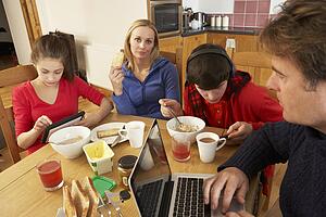 Teenage Family Using Gadgets Whilst Eating Breakfast Together In Kitchen