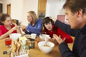Parents Taking Away Gadgets From Children Whilst Eating Breakfast Together In Kitchen