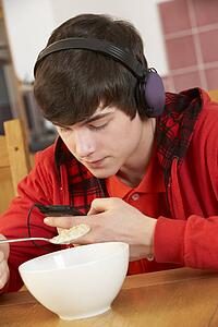 Teenage Boy Listening To MP3 Player Whilst Eating Breakfast
