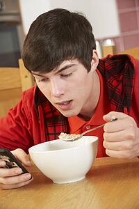 Teenage Boy Teenage Texting Whilst Eating Breakfast