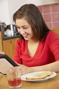 Teenage Girl Using Tablet Computer Whilst Eating Breakfast