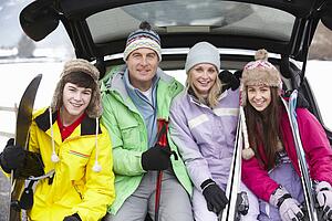 Teenage Family Sitting In Boot Of Car With Skis
