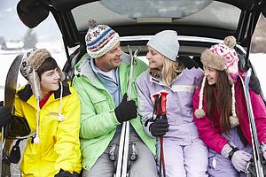 Teenage Family Sitting In Boot Of Car With Skis
