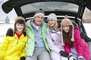 Teenage Family Sitting In Boot Of Car Wearing Winter Clothes