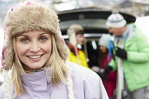 Mother Smiling At Camera Whilst Family Load Skis In Boot Of Car