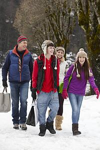 Teenage Family Carrying Shopping Walking Along Snowy Street