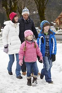 Family Walking Along Snowy Street In Ski Resort