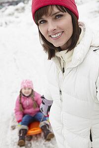 Mother Pulling Daughter On Sledge Along Snowy Street In Ski Resort