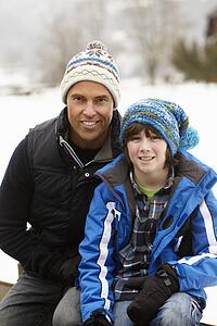 Portrait Of Father And Son Wearing Winter Clothes In Snowy Landscape