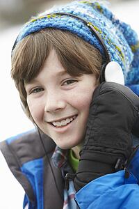Boy Wearing Headphones And Listening To Music Wearing Winter Clothes In Snowy Landscape