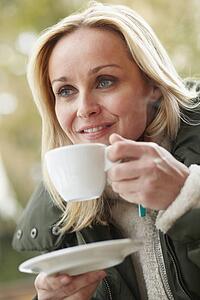 Woman In Outdoor CafÃ© With Hot Drink Wearing Winter Clothes