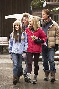 Teenage Family Walking Along Snowy Town Street In Ski Resort