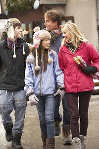 Teenage Family Walking Along Snowy Town Street In Ski Resort